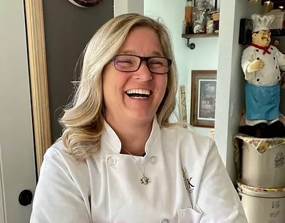 image of a woman standing in her kitchen smiling, possibly even laughing
